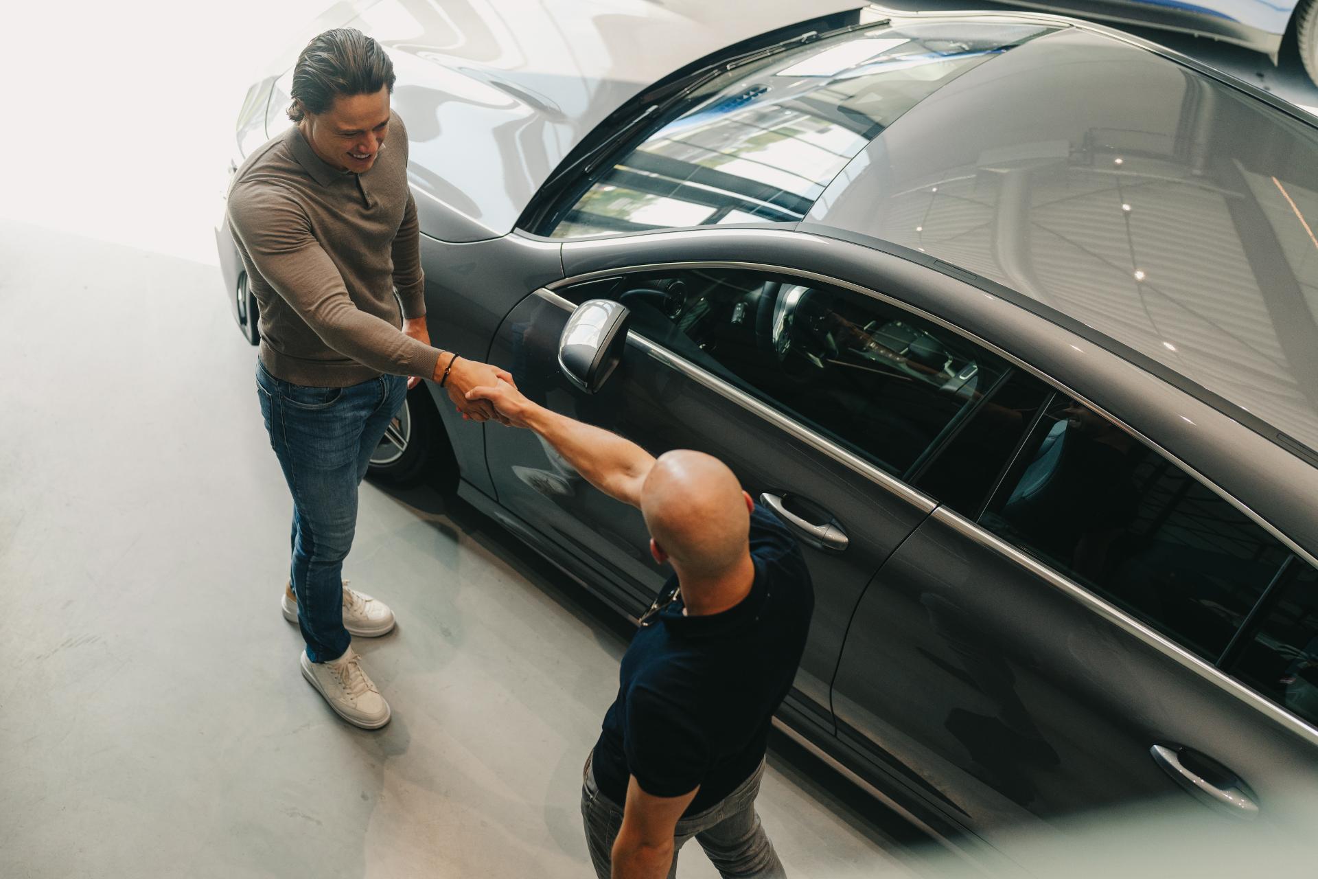 Verkoper en klant schudden elkaar de hand na aankoop van een luxe auto	