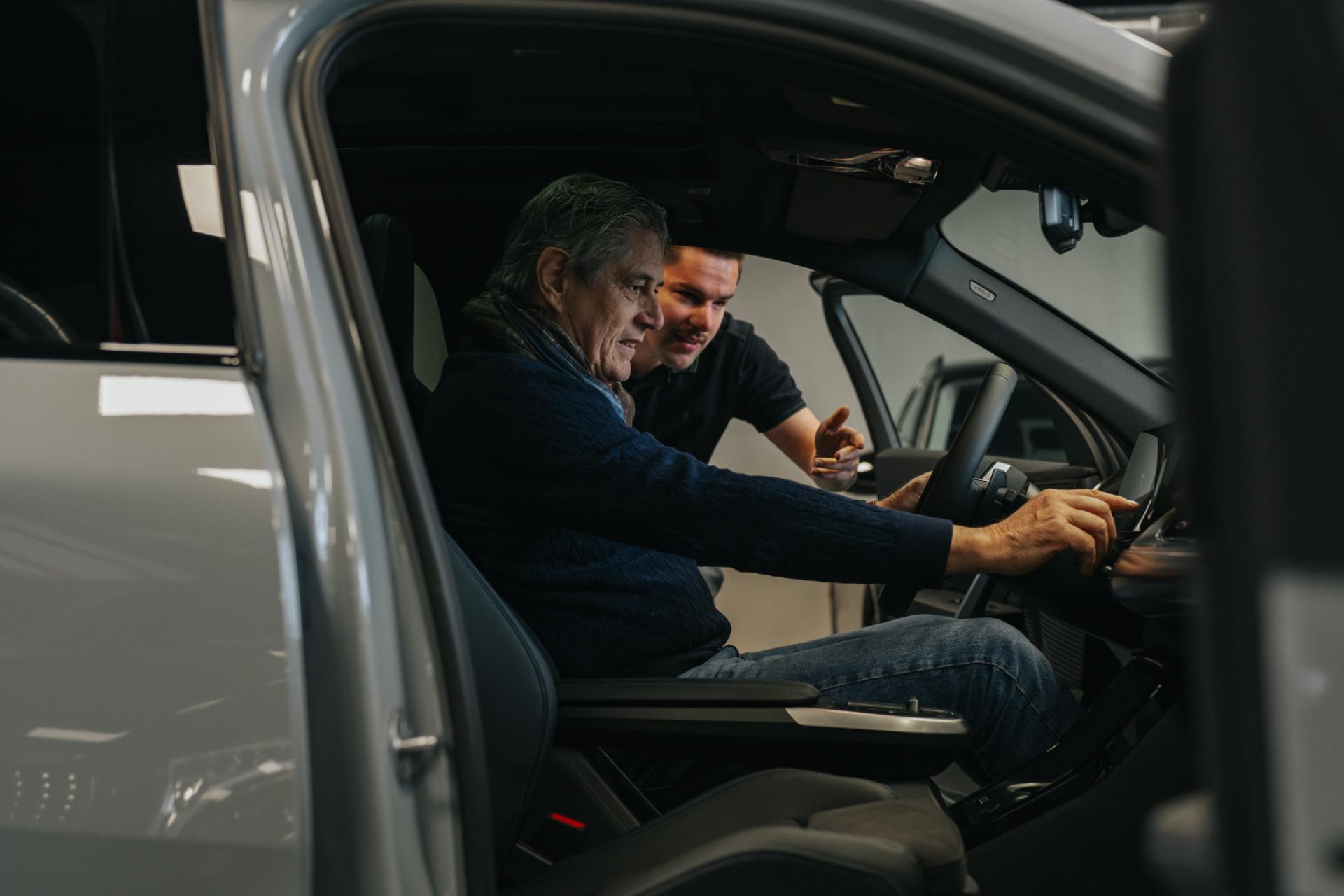 lant krijgt uitleg over interieur en dashboard van wagen in showroom